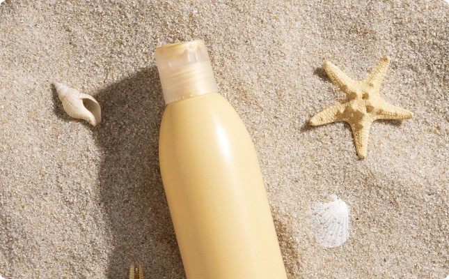 Crema solar en la arena con una estrella de mar y una almeja al lado