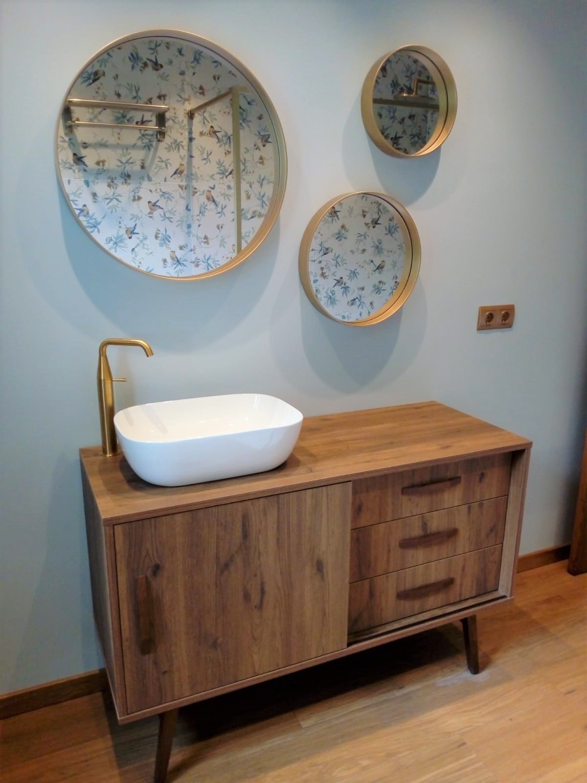 Baño reformado con tres espejos redondos en la pared y mueble de madera